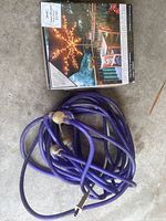 Coiled purple rope light with plug, lying on a floor surface, along with the patio umbrella lights box.