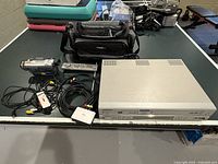 Samsung DVD-V2500 DVD/VHS player unit alongside cables and adapters with black carrying case on table