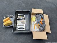 Photo showing three metal grout floats with black handles, a large black plastic tray, and three yellow sponge floats in a metal tray.