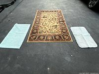 Photo of the traditional oriental rug centered with two light blue bath mats placed on both sides on dark asphalt showing full set and condition