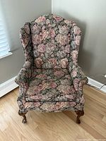 Front view of the wingback armchair showing the floral upholstery and wooden legs.