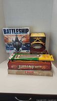Front view of five board games stacked including Battleship, treasure chest game, cribbage, Jumanji and Risk
