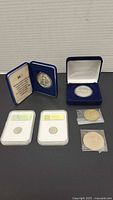 Overview image showing 7 coins: 2 boxed commemorative coins, 2 sample 1964 D 10 cent coins in plastic holders, 2 large coins in individual plastic sleeves.