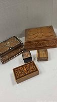 Five decorative wood boxes in varying sizes and designs placed against a white backdrop showing variety in carving and inlay.