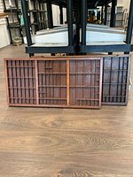 Front view of two wooden display trays leaning against a plastic stand, showing multiple rectangular compartments.