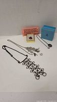Photo showing a variety of jewelry including a black metal abstract geometric necklace, a sterling silver locket necklace, a silver metal floral pendant necklace, a floral brooch, and a ring in a box.