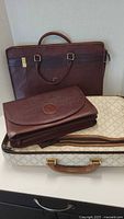 Three ladies briefcases showing the Bally red leather briefcase at back, large red leather purse in front, and white patterned hard briefcase underneath.