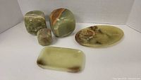 Five pieces of green onyx decorative stone blocks and stone trays arranged together on a white background, showing color and pattern variation.