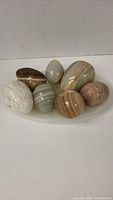 Seven polished eggs arranged standing on an oval transparent tray showing different colors and stone patterns.