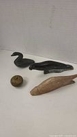 Four small indigenous stone sculptures including two dark grey birds, a seal, a rounded spiral carved stone, and one lighter brown elongated bird sculpture.