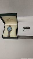 Sarelle Collection wristwatch with a light blue dial in original box, with Sarelle tag beside it on white surface.