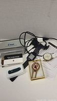 Photo showing all items together including Garmin watch, Geneva watch, Victorinox cutter in box, money clip in gold-tone box, and Pilot pen
