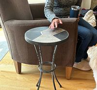 Full view of the accent table next to a chair for scale, showing stone top and twisted metal legs.