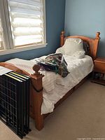Twin wooden bed frame with white bedding and some items on the bed, including a mattress frame leaning against it