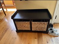 Front view of wooden bench showing the two rattan baskets positioned inside the compartment below the tray-like top surface.
