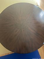 Top-down view showing the rich dark wood with starburst veneer pattern on the round tabletop.