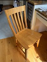 Wooden PotteryBarn desk chair with slatted back and contoured seat, placed on wooden floor next to kitchen counters.