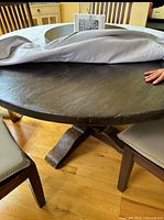 Photo of round wooden dining table with dark finish and pedestal base, showing scratches and wear.