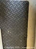 Close-up photo of textured black rubber surface showing embossed chevron and diamond patterns, minor scuffs visible.