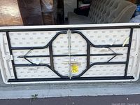 Underside view of white plastic folding table showing metal support legs and folding mechanism.