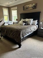 Photo of the king size wooden bed frame in a bedroom setting with bedding and pillows, showing the tall headboard and footboard in black wood.