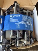 First Alert escape ladder folded with blue securing strap inside a cardboard box