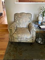 Front view of the floral upholstered armchair showing curved back, rolled arms, and nailhead trim with wooden caster legs.