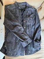 Front view of the jacket laid flat showing zippered pockets, button closures, and cuffs.