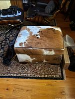 Brown and white cowhide ottoman viewed frontally showing top cushion and sides.