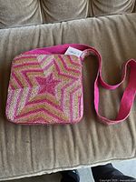 Front view of the purse showing pink, gold, and silver beaded star pattern and pink strap.