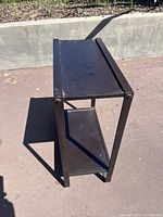 Side view of a small black metal outdoor table showing two shelves and rust spots.