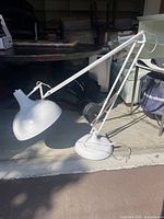 White adjustable standing lamp with articulated arm and dome-shaped shade lying on the floor in a garage setting.