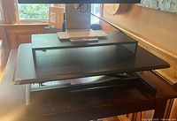 Front view of the black adjustable sit-stand desk converter on a wooden desk with monitor and keyboard setup.