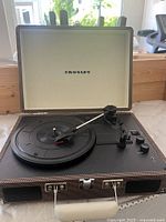 Open Crosley portable record player showing black turntable, tonearm, control knobs, and interior lid with Crosley logo.