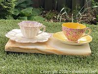 Two antique teacup and saucer sets displayed on a wooden board on grass.