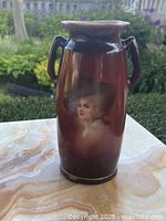 Front view of antique ceramic vase showing painted portrait of a woman wearing a hat, with reddish-brown glaze and double handles.