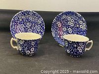 Two blue and white floral teacups with matching saucers from side angle.