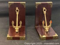 Front view of two wooden bookends with brass anchor decoration and brass corner plating.