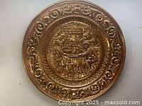 Full view of round brass wall plate with embossed detailed scene and ornamental border
