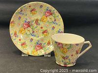Teacup and matching saucer with chintz floral pattern of roses and small blue flowers on yellow background, displayed upright