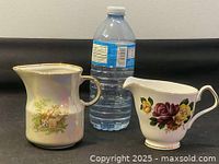 Two ceramic creamers side by side with a water bottle for scale.