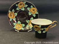 Teacup and saucer set showing the floral design against a black background with yellow roses and green leaves