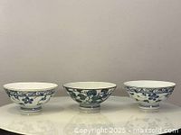 Front view of three Japanese blue and white porcelain bowls, showing floral and scroll pattern decoration, placed side by side