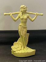 Front view of yellow glazed porcelain statue of woman holding bamboo pole horizontally.
