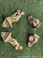 Four plaster wall decor pieces arranged on grass, including two cherubs and two ornate brackets