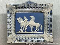 Full view of the porcelain hanging decor showing rectangular plaque with ornate white framing and central relief of horses and rider on blue background.