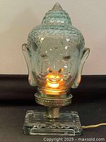 Front view of illuminated Buddha head glass lamp showing details and glow inside the head.
