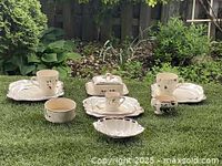 Full view of two Staffordshire lunch sets placed on grass, showing all pieces including plates, cups, bowels and covered dish with black butterfly decorations