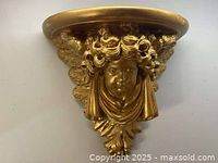 Front view of vintage cherub wall shelf showing detailed cherub face and wings in gold finish.