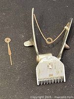 Front and side view of metal vintage Oster animal clipper with attached spring, serrated blade, and small flat key placed beside it.